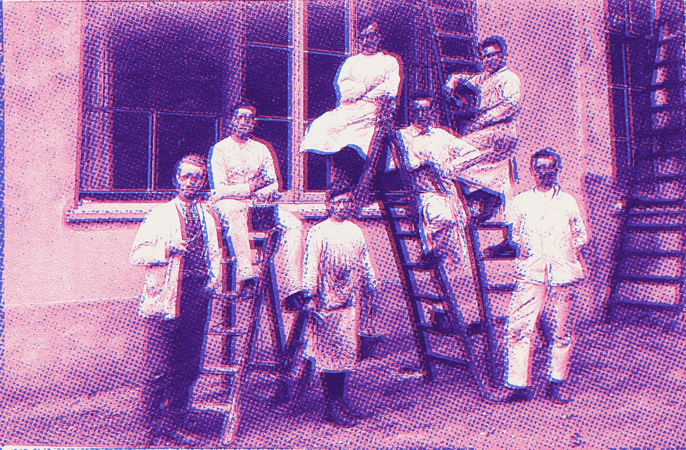 Zeven schilders in witte jassen met ladders en verfemmers voor een gevel, historische foto van het schildersbedrijf Hendrixen
